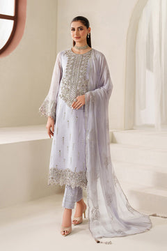 Woman wearing a light gray traditional outfit with silver embroidery in a bright room.